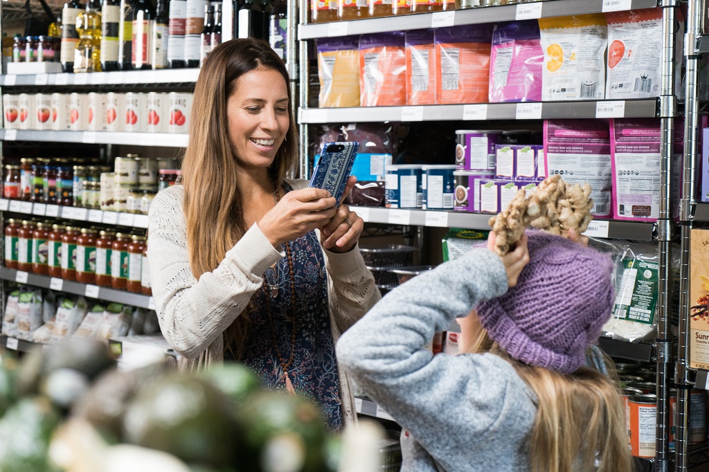 An image of a parent using a cellphone camera to take a picture of a child in in a store